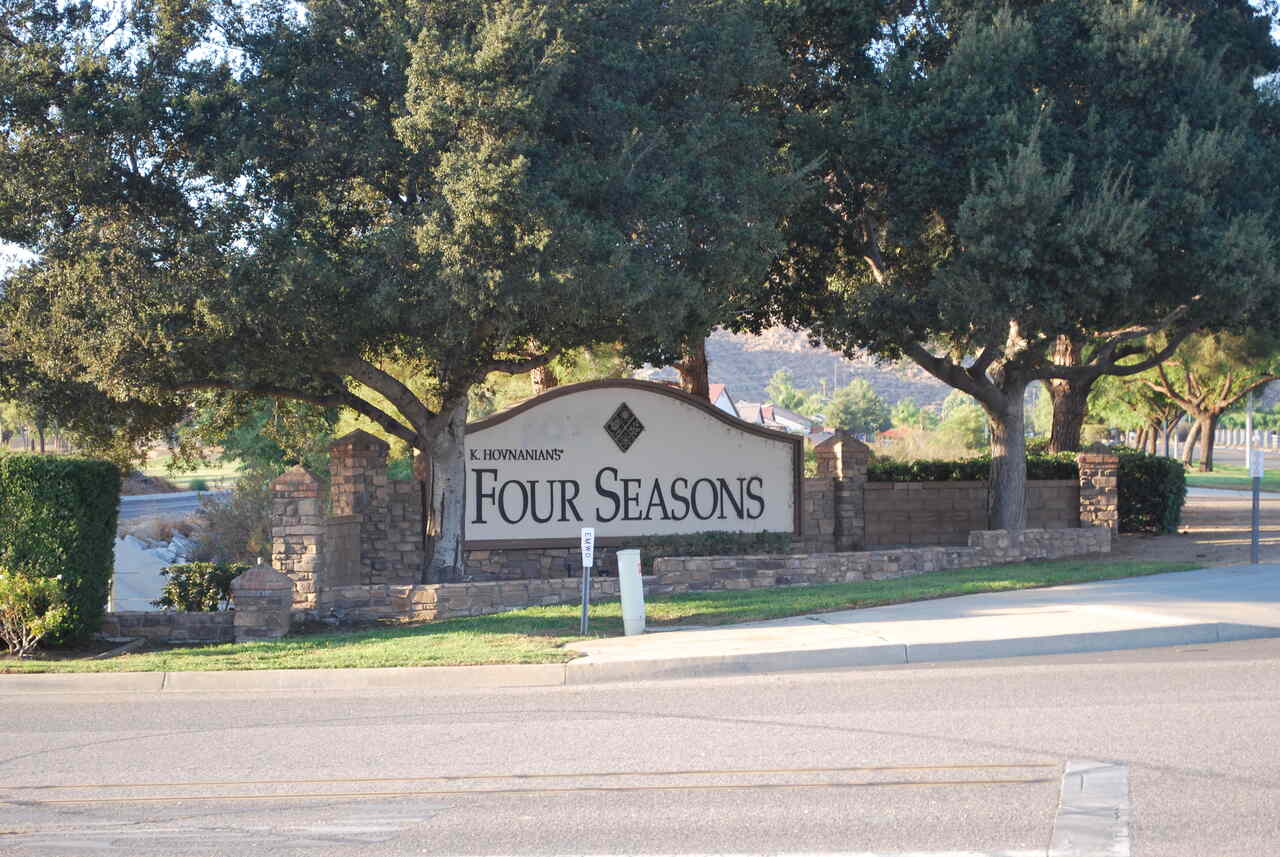 Four Seasons Community Highway 74 California Ave Hemet CA Four Seasons" community entrance sign by K. Hovnanian, framed by mature oak trees and a stone wall with mountains in the distance — about a block north of Highway 74 and California Ave, near The Laundry Basket in Hemet, CA.